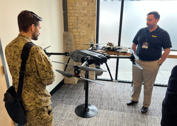 A man displaying a drone device to an armed forces personnel